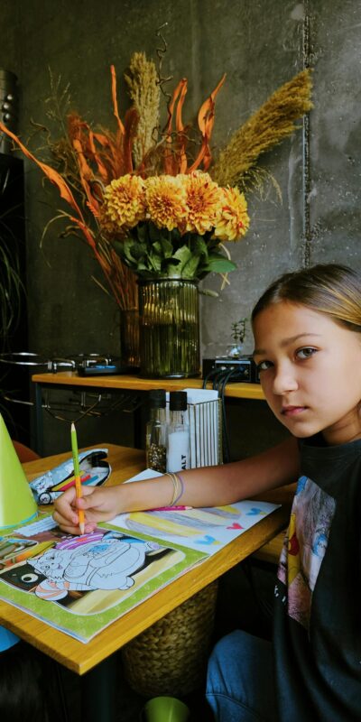 Photo of a Girl Drawing at a Desk, and a Yellow Bouquet in Background